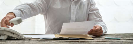 Unidentified business man picks up receiver and holds document as he dials.の写真素材