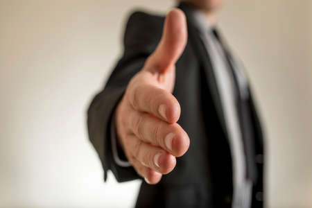 Close-up view of businessman hand reached out to handshake. Incognito man in suit blurred in background.の写真素材