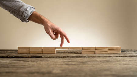 Man hand showing walking fingers over fragile bridge of wooden bricks on table surface on sepia toned background, concept with copy space.の写真素材
