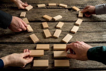 Business teamwork and bright ideas concept with a group of business people arranging wooden blocks into the shape of a light bulb on an old rustic table, close up view of their hands.の写真素材