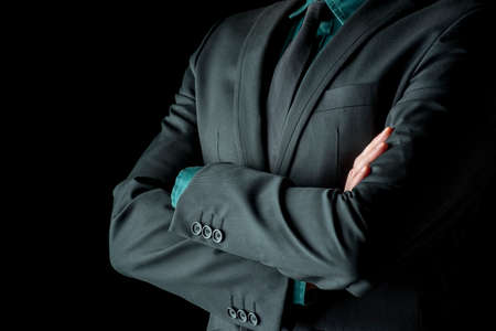 Closeup view of the torso of a businessman standing with folded arms in a classic black suit with a green shirt and necktie, depicting confidence, success and authority.の写真素材