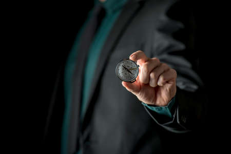 Close-up view of hand showing little round compass to camera, with incognito man in suite in soft focus, isolated on black background.の写真素材