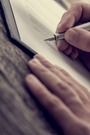 Close-up view of man hands with fountain pen ready to put a signature on document over wooden table surface.の写真素材