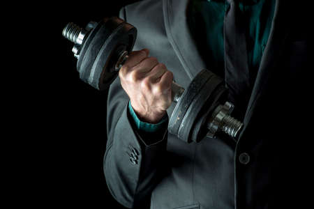 Businessman in formal suit lifting weights. Concept of power and determination in business. Over black background.の写真素材