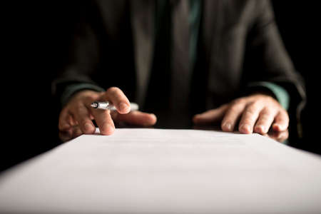 Businessman in business suit holding a fountain pen on a signed contract or document over black background.の写真素材