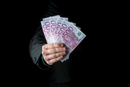 Businessman holding a fistful of 500 euro banknotes extended to the camera conceptual of wealth, success or payoff, cropped closeup over black background.の写真素材