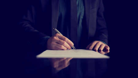 Retro image of businessman signing document or contract with silver pen on a black desk with...