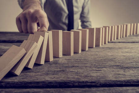 Retro vintage style image of a businessman stopping domino effect. Saving business concept.の写真素材