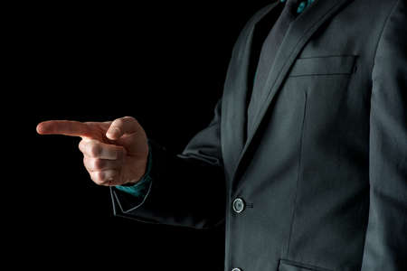 Incognito adult man pointing forward or left with his index finger, standing in business black suite isolated on black background.の写真素材