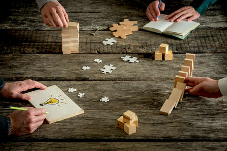 Businessmen sharing ideas concept. Close-up full frame image with hands of four people over rough wooden table, with dominoes effect, drawing light bulb, puzzle pieces and other conceptual stuff.の写真素材