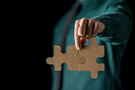Close-up view of hand holding two matching puzzle pieces, with figure of incognito person in soft...