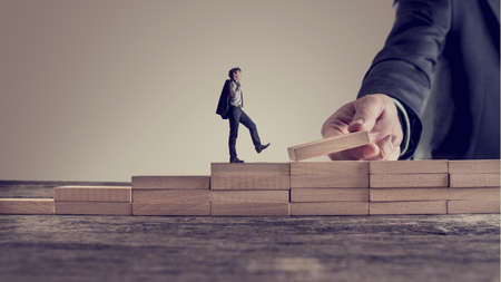 Retro vintage style image of a business person walking up steps, while the hand of other man building stairs for him in a conceptual image of personal and career promotion, leadership and opportunity.の写真素材