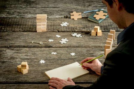 Rare view of blank notebook with copy space in front of businessman, hands with pencil over old rough wooden table surface with puzzle pieces,dominos, notebook and other conceptual stuff.の写真素材