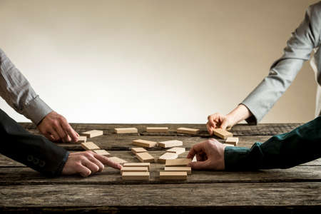 Business people arranging wooden blocks into the shape of a light bulb on a rustic table,...
