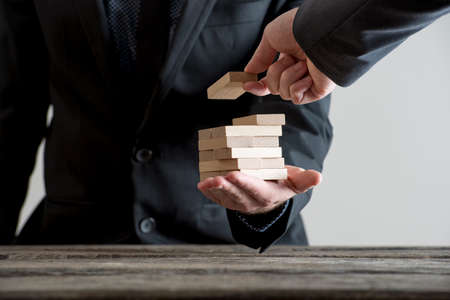 Close-up man hand in suite placing wooden domino bricks in stack on other businessman open palm over...