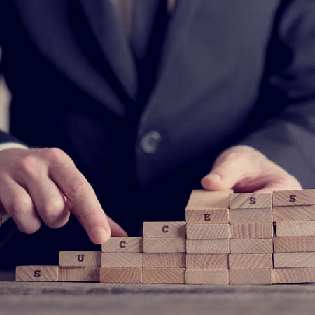 Close-up of businessman building career ladder stairs or growing graph concept of wooden domino bricks with SUCCESS sign letters, toned retro effect.の写真素材