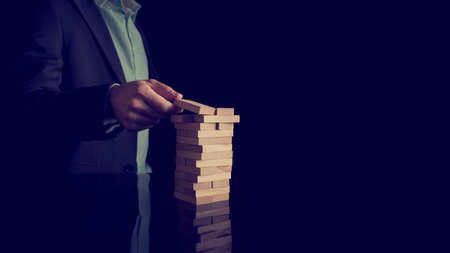 Businessman building a tower of stacked blocks of wood in a conceptual image, retro effect faded look.の写真素材