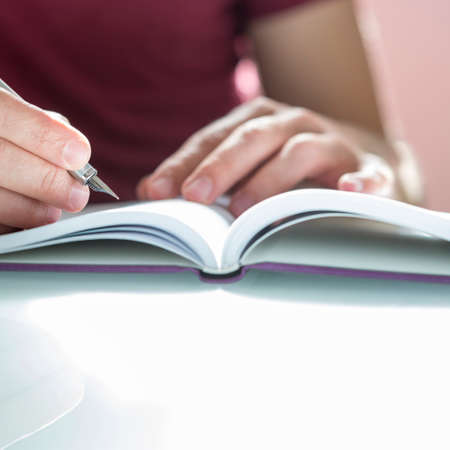 Closeup of a male hand writing on notepad with silver fountain pen on a white desk.の写真素材