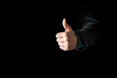 Hand of a businessman wearing black business suit showing thumb up, sign of approval, on black background.の写真素材