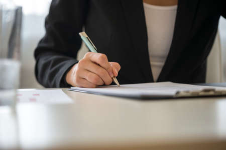 Low angle view of a woman signing contract or subscription form with a pen on white desk.の写真素材