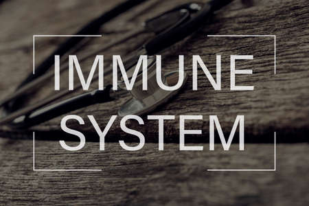 Immune system text over medical stethoscope with black tubes lying on textured wooden boards.の写真素材