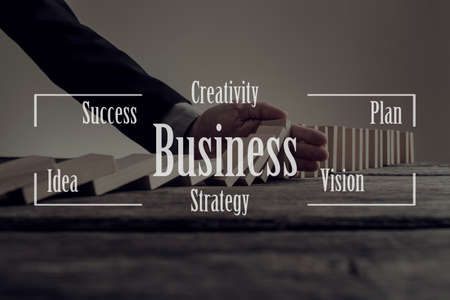 Conceptual business text over image of a businessman preventing dominoes from crumbling with palm on an old wooden table.の写真素材