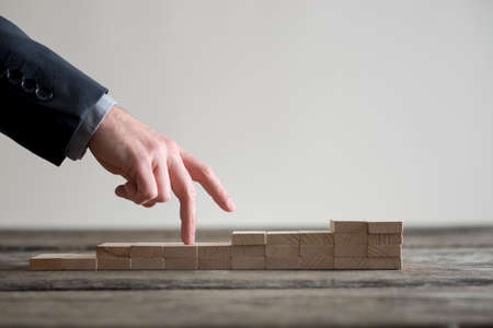 Male hand in business suit walking its fingers up a staircase made of wooden blocks.の写真素材