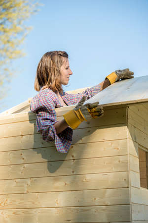 Woman wearing protective gloves working on roof of tree house outdoors.の写真素材