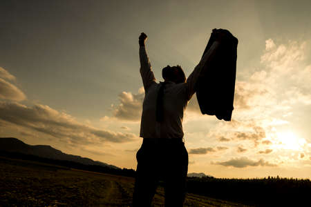 Silhouette of a businessman raising his arm while looking up the sky for success.