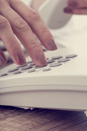 Retro effect faded and toned image of a female hand dialing a telephone number using white landline phone.の写真素材