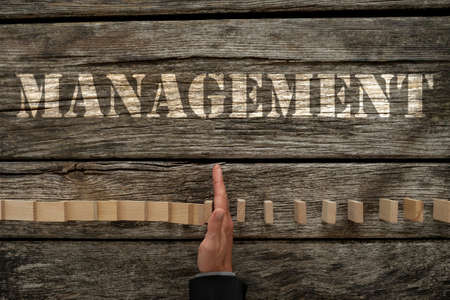 Top view of male hand in business suit stopping falling dominos on a textured wooden desk with...