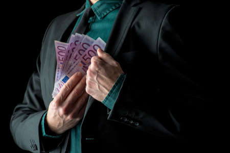 Businessman in black suit holding 500 euro bills near inside pocket of his jacket.の写真素材