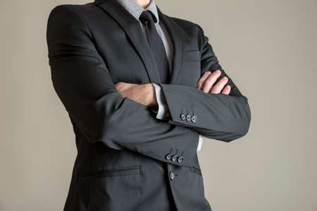 Torso of a businessman standing with folded arms in a classic black suit, depicting confidence and authority.の写真素材