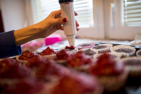 Woman decorating cupcakes with raspberry frosting.