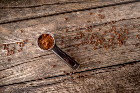 Top view of coffee machine filter holder with flavored ground coffee and beans on old wooden table.