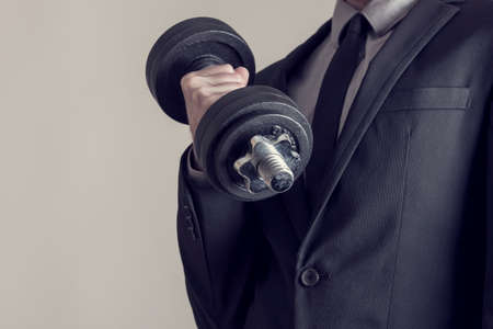 Retro effect faded and toned image of a businessman doing dumbbell biceps curl wearing a formal suit.の写真素材