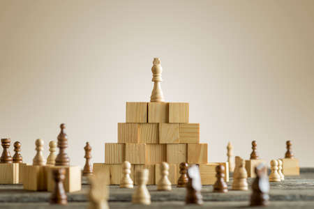 White king on wooden building blocks with other arranged various chess pieces under the pyramid.の写真素材