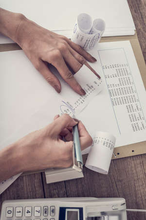 Retro image of accountant working at her desk checking figures on an adding machine, high angle...