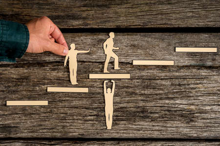Teamwork concept on rustic wood with group of silhouette cutouts and a male hand helping a paper...