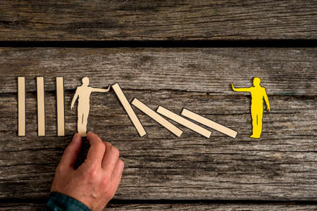 Unidentifiable adult man using his hand and carefully positioning small white leaning wooden figure next to blocks and yellow wood figureの写真素材