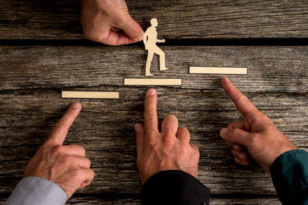 Business teamwork and cooperation concept with the hands of four businesspeople supporting paper cut outs of a man climbing the steps to success over rustic wood background.の写真素材