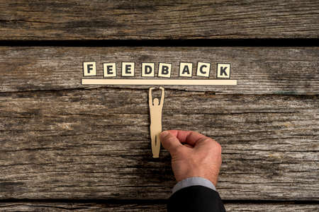 Unidentifiable adult man using his hand to position small human figure holding up paper bar with the word feedback.の写真素材