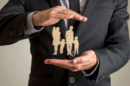 Businessman protecting family silhouette with a father, mother, baby and two children with his cupped hands in conceptual image of life insurance and security.の写真素材