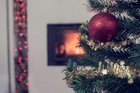 Christmas background with a red bauble on a tree decorated with sparkling tinsel with a burning fire in the background, vintage effect toned image.の写真素材