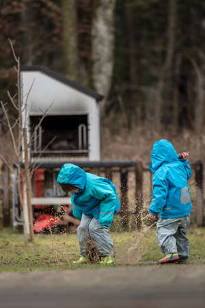 Two children wearing blue jackets playing outdoors in puddle.の写真素材