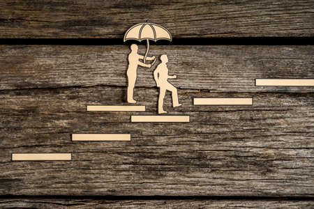 Two small people silhouette walking up stairway as one holds an umbrella over the other as they walk over wood background.の写真素材