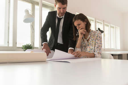 Experienced businessman analyzing important blueprints together with a worried female investor or...