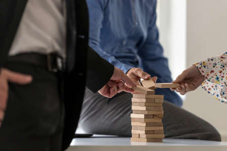 A close up of a group of colleagues in an office carefully building a tower of wood blocks on a table, teamwork concept.の写真素材