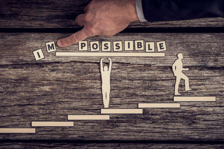 Teamwork concept making the Impossible Possible with two paper cutouts of men, one supporting the...