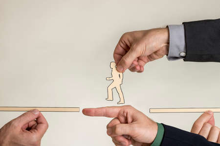 Business teamwork and success concept with a team of businesspeople holding paper cutouts of a man walking crossing a bridge formed by a finger with copy space.の写真素材